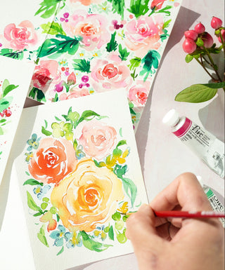 Floral watercolor designs on paper with a hand holding a red pen.