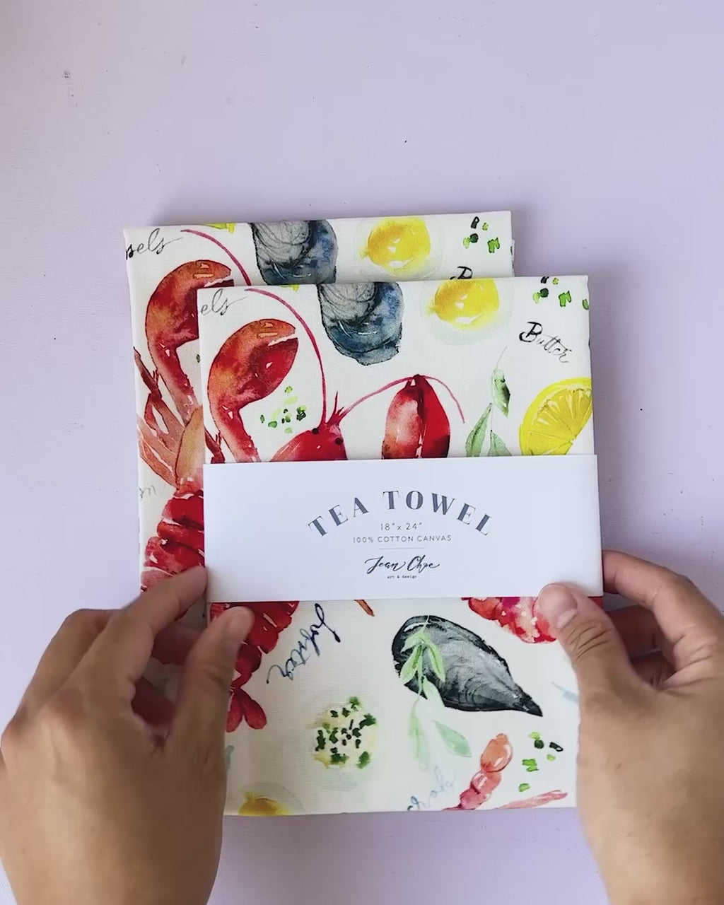 Video showing Jean Choe's cotton canvas tea towel with vibrant watercolor seafood table including lobsters, crabs and clams